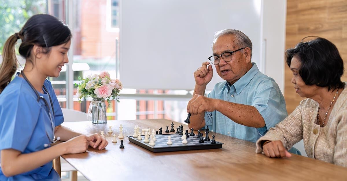 Healthcare professional playing chess with two elderly patients